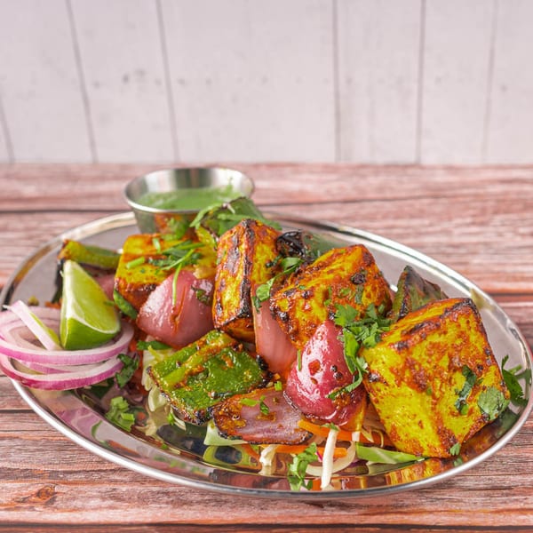 Indian paneer tikka with red onions, green peppers, lime, and cilantro on a silver platter.