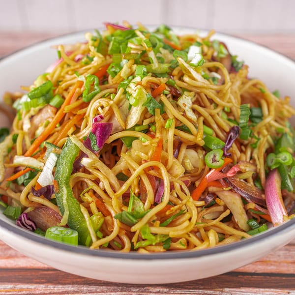 Close-up of Indian noodles with mixed vegetables, including carrots, cabbage, and green onions.