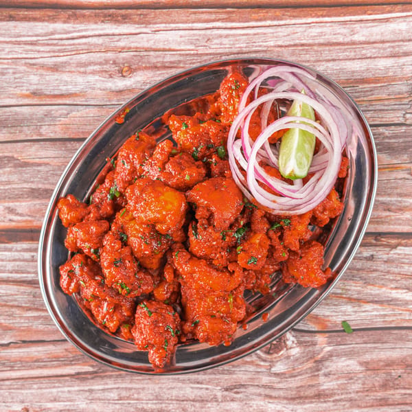 Bright red Indian chicken 65, garnished with sliced red onions and a lime wedge, on a silver platter.