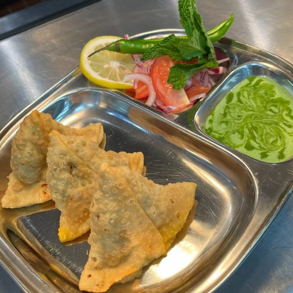 Crispy samosas, fresh salad with lemon and mint, and green chutney on a metal tray.