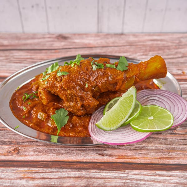 Indian chicken curry with a drumstick, garnished with cilantro, lime, and red onion slices.