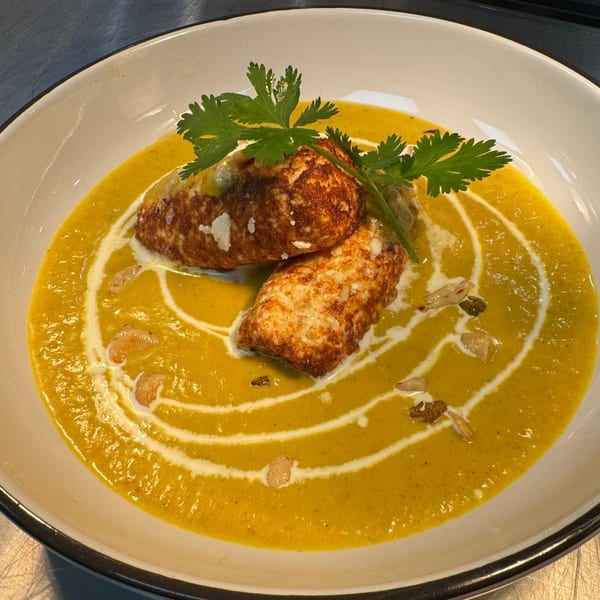 Two fried paneer pieces in a yellow curry with cream swirls and cilantro garnish.